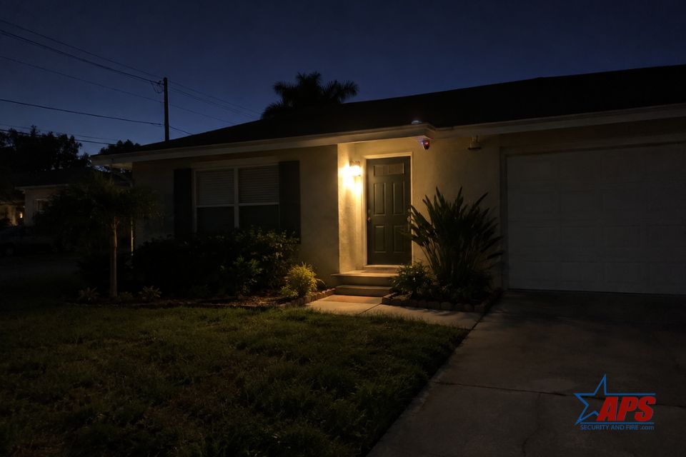 A modern home security system interface displaying a surveillance camera feed on a tablet, with the backdrop of a house at dusk